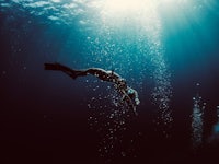 a person is diving under the water with a light shining on them